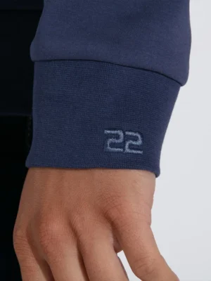 Detalle del logotipo Code 22 en el puño de la sudadera azul