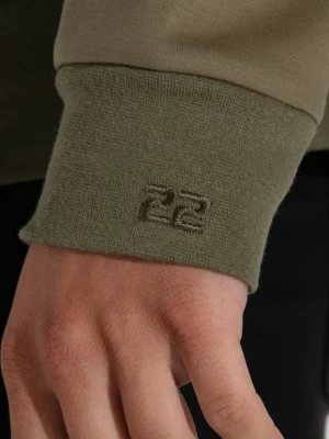 Detalle del logo Code 22 en el puño de la sudadera verde para un toque distintivo.