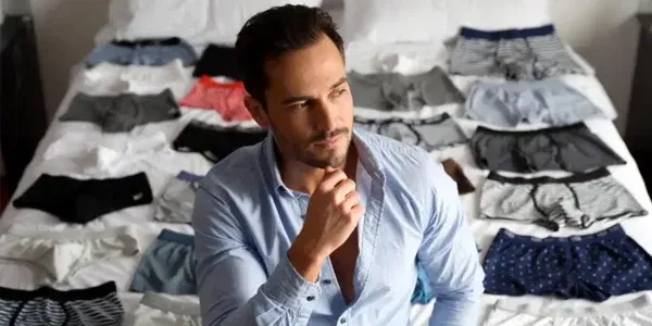Hombre pensando cuántos calzoncillos necesita con muchos calzoncillos sobre la cama