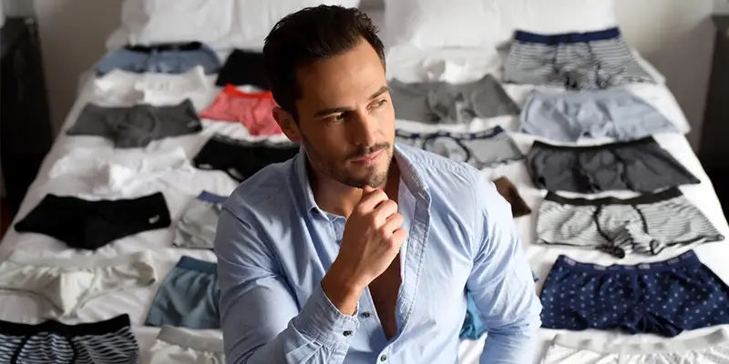 Hombre pensando cuántos calzoncillos necesita con muchos calzoncillos sobre la cama