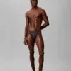 Hombre llevando calzoncillo slip Calvin Klein CK Black de talle bajo en color marron oscuro carbón