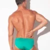 Modelo de espaldas de cuerpo entero con bañador mini slip Code 22 Amsterdam verde