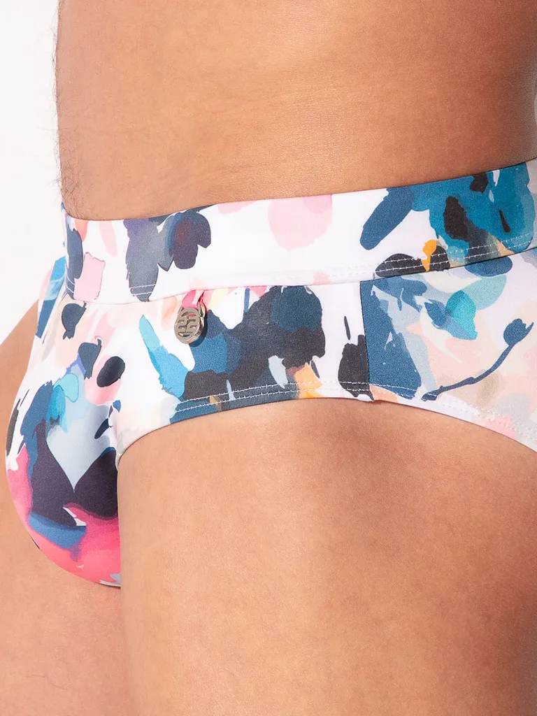 Primer plano medallón metálico Code 22 grabado en cintura lateral bañador slip London estampado floral